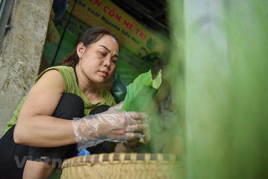 50-летняя продавщица «ком» Нгуен Тхи Лань говорит: «Уже более 20 лет я продаю «ком» производства деревни Вонг. «Ком» этой деревни очень вкусный, ароматный и липкий. По цвету можно узнать, добавляли или нет в продукцию химические вещества. Если «ком» имеет бледно-зеленый цвет, то он – натуральный, а если яркий зеленый – то это означает, что в него добавлены химические вещества. «Ком» в этом сезоне продается по 250 тысяч донгов за килограмм. Я использую листья лотоса для упаковки «ком». Выручка от продажи «ком» небольшая, а при этом работа – очень нелегкая из-за постоянно меняющихся погодных условий. Однако благодаря любви к этому делу я все ещё продолжаю продавать «ком» на рынке и на улицах города». (Фото: Vietnam+)