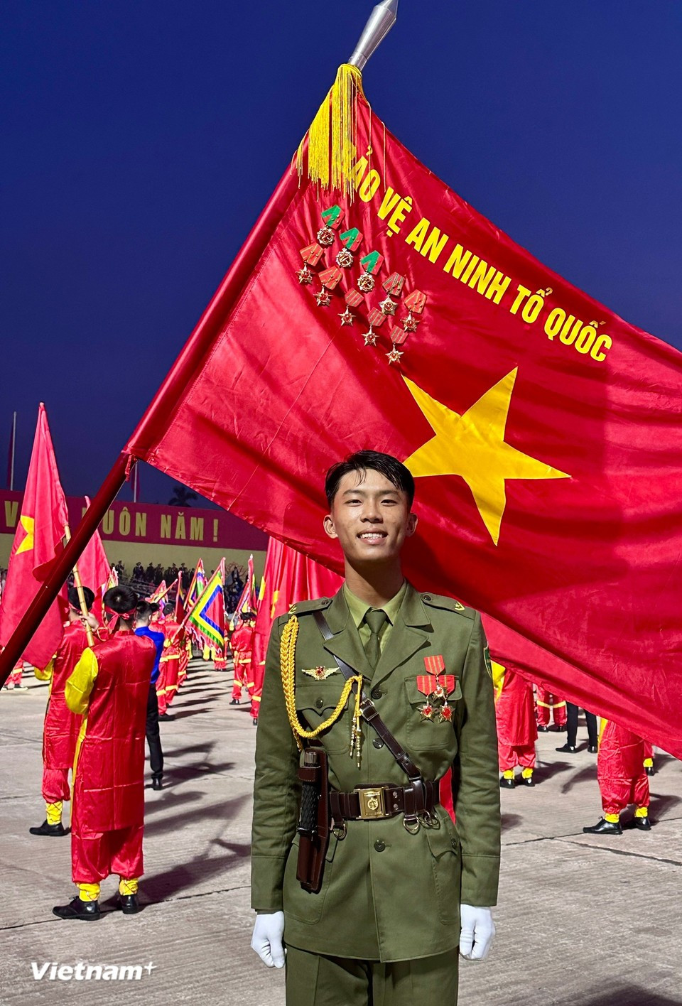 Молодой солдат сияет гордостью рядом с красным флагом со звездой. (Фото: Vietnam+)