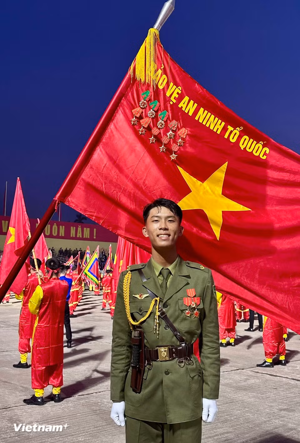 Молодой солдат сияет гордостью рядом с красным флагом со звездой. (Фото: Vietnam+)